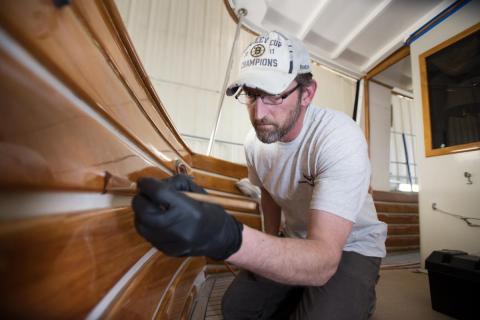 Technician applying new paint and varnish to a boat Technician applying new paint and varnish to a boat